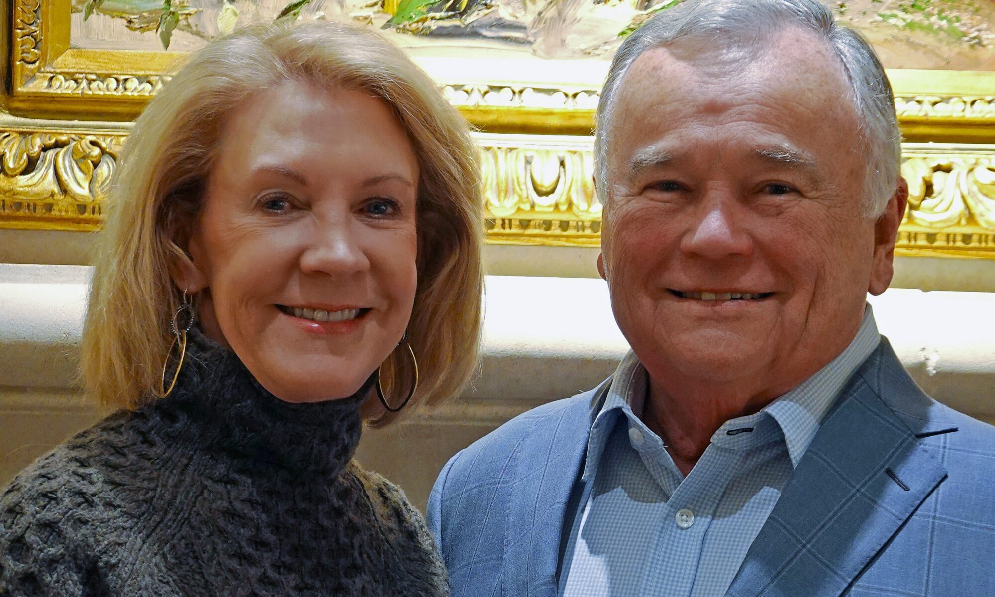 Janeen and Bill Lamkin pose together while smiling in front of a piece of art
